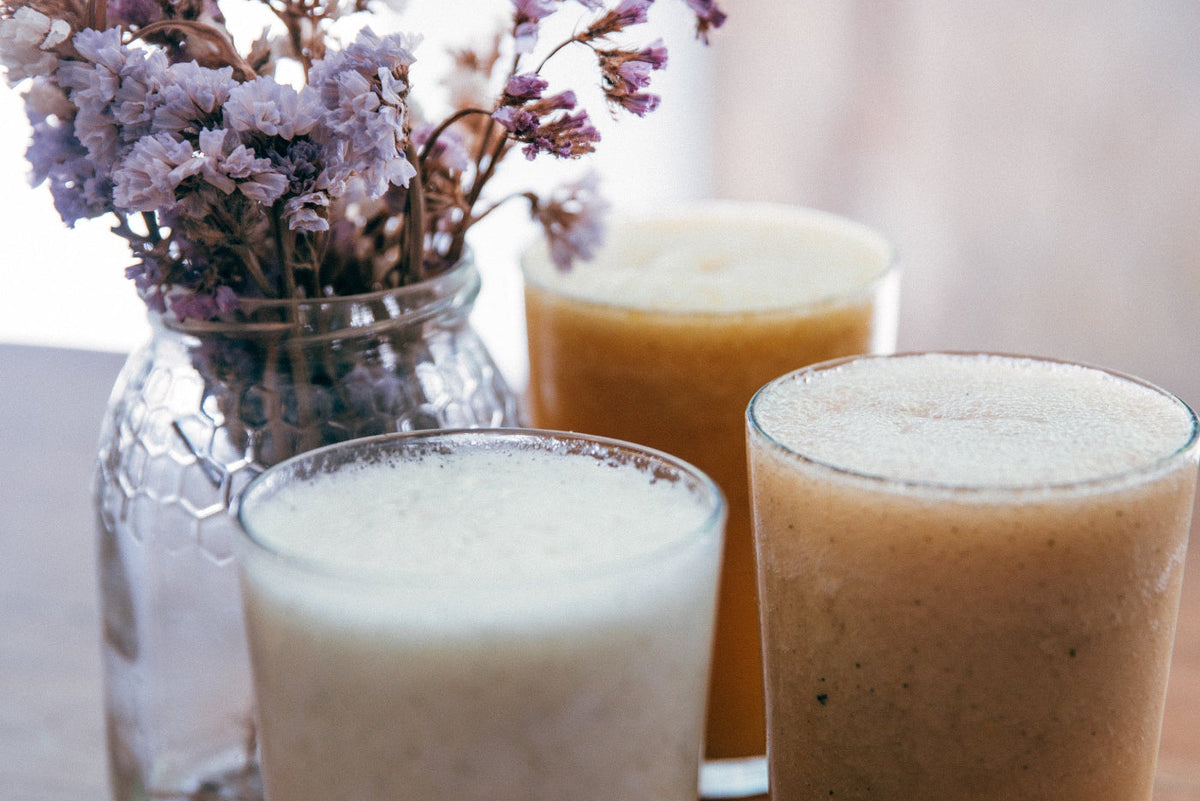 three different types of beverages next to a mason jar type vase with small lilac and white flower buds